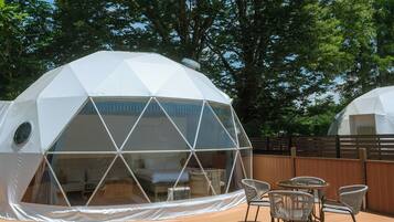 A geodesic dome structure with a transparent section revealing a bed and a small table with chairs.