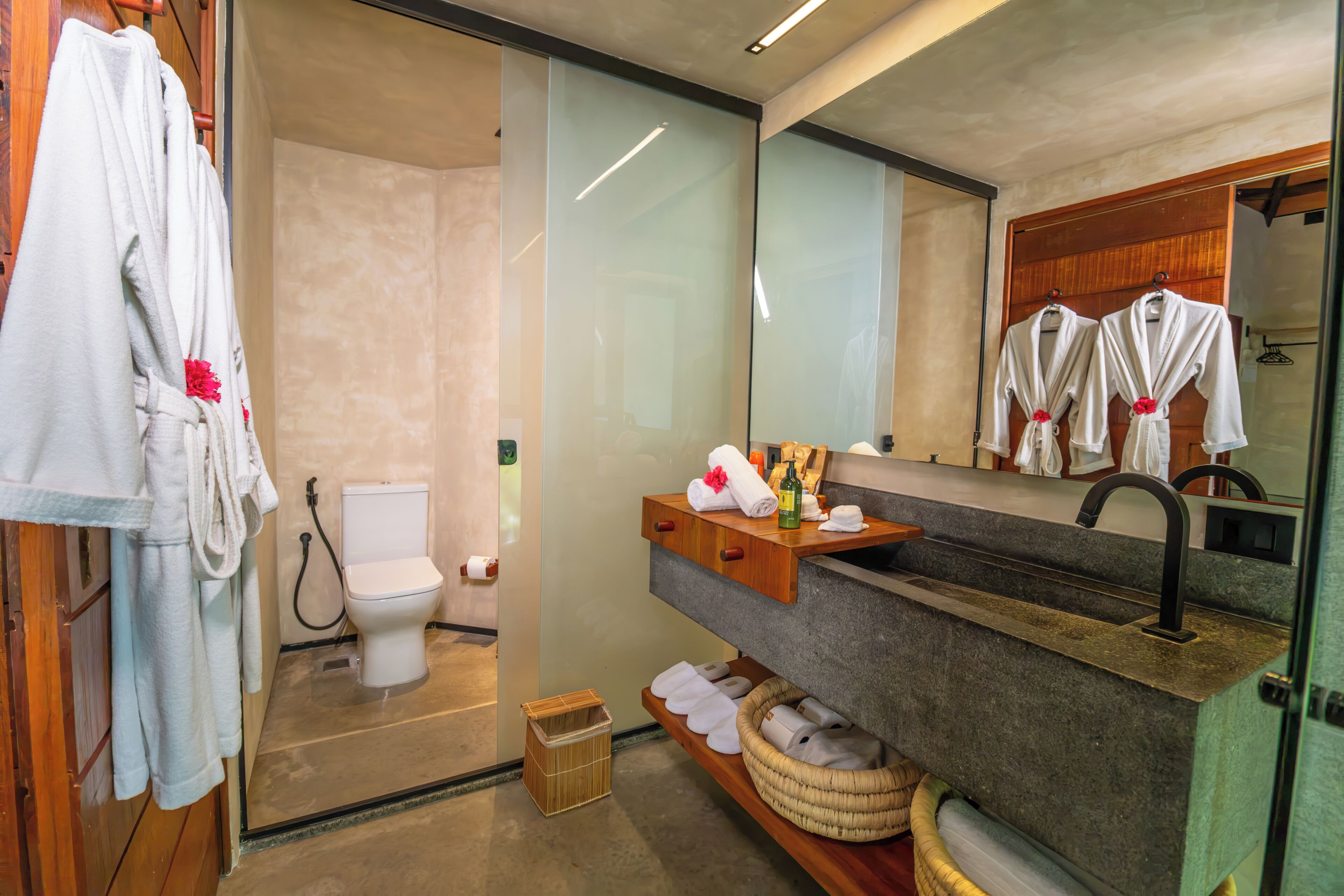 A modern bathroom with a glass shower enclosure, a toilet, a vanity with a mirror, and a shelf with towels and toiletries.
