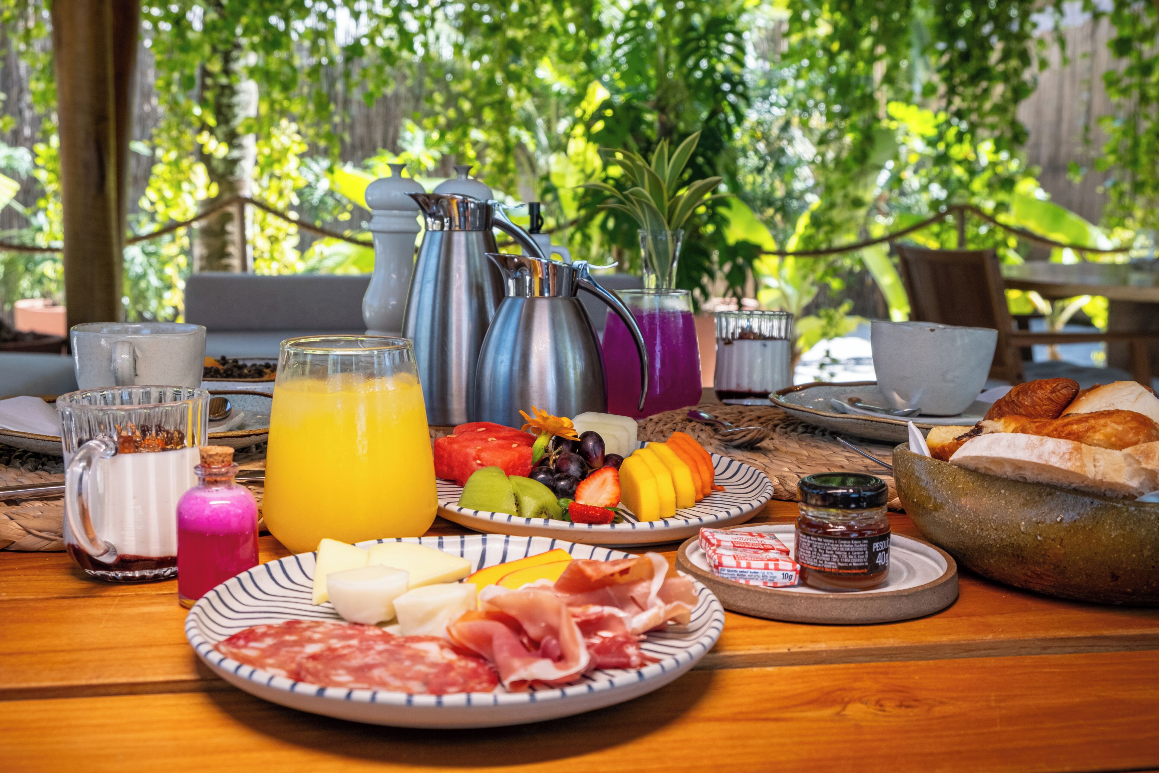 Une table de petit-déjeuner avec des assiettes remplies de nourriture, une cafetière et un verre de jus d’orange.