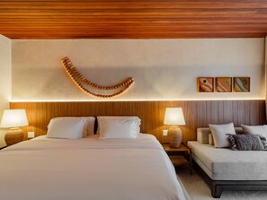 A hotel room with a large bed, two bedside tables with lamps, a sofa, and a wooden ceiling.