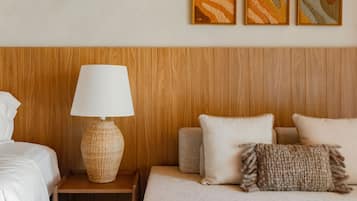 Un dormitorio con cabecera de madera, mesita de noche con lámpara, cama con almohadas y tres cuadros enmarcados en la pared.