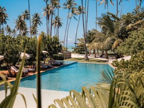 A pool area with lounge chairs and palm trees, surrounded by greenery and a view of the ocean. - NANNAI Milagres (Passo de Camaragibe)