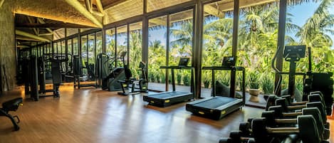 Un gimnasio con equipo de ejercicio, ventanas amplias y suelo de madera.