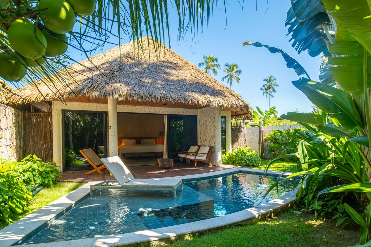 A poolside area with a thatched-roof structure, lounge chairs, and a swimming pool.