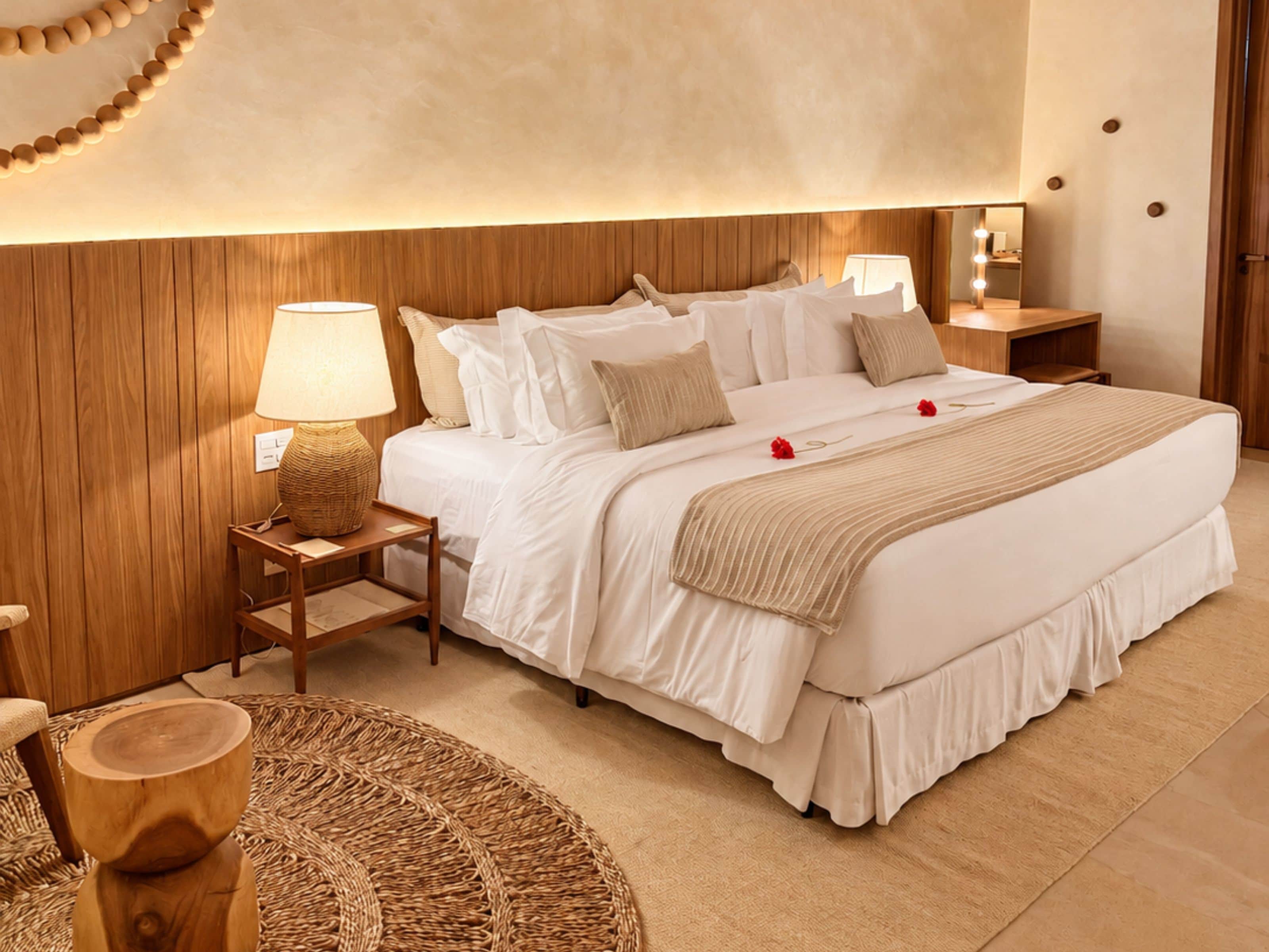 Una habitación de hotel con una cama grande, cabecera de madera, lámparas de noche y un espejo con luces.