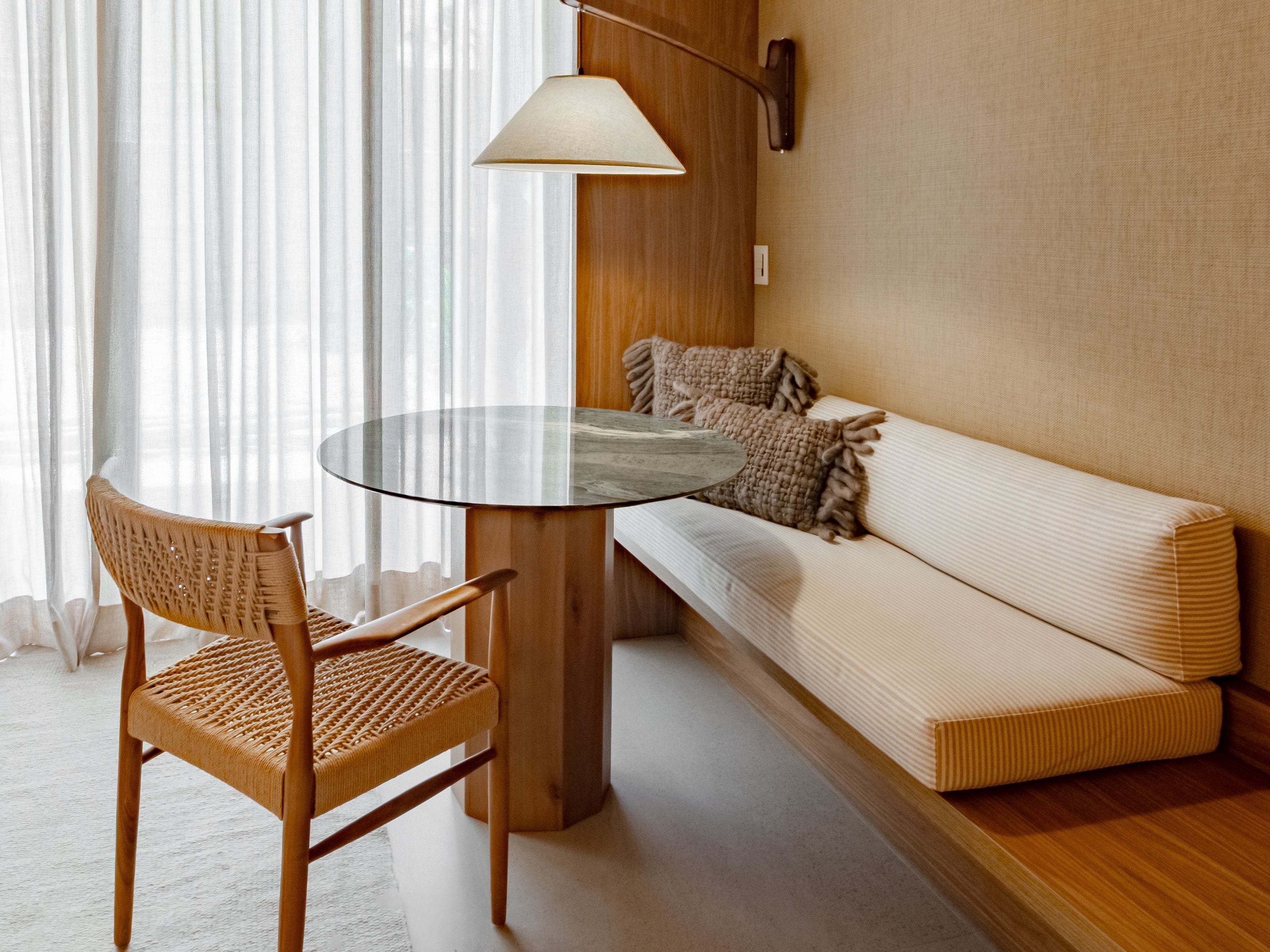 Une pièce comprenant une table ronde en verre, une chaise en osier, un canapé avec des coussins et une lampe fixée au mur.