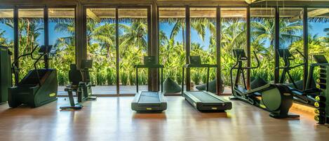 Un gimnasio con equipo de ejercicio y amplias ventanas con vistas a palmeras.