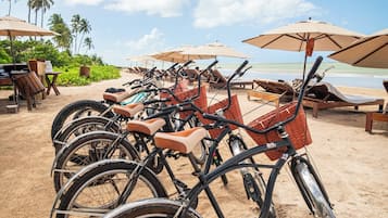 Des vélos sont garés sur une plage de sable, avec des parasols et des chaises longues en arrière-plan.