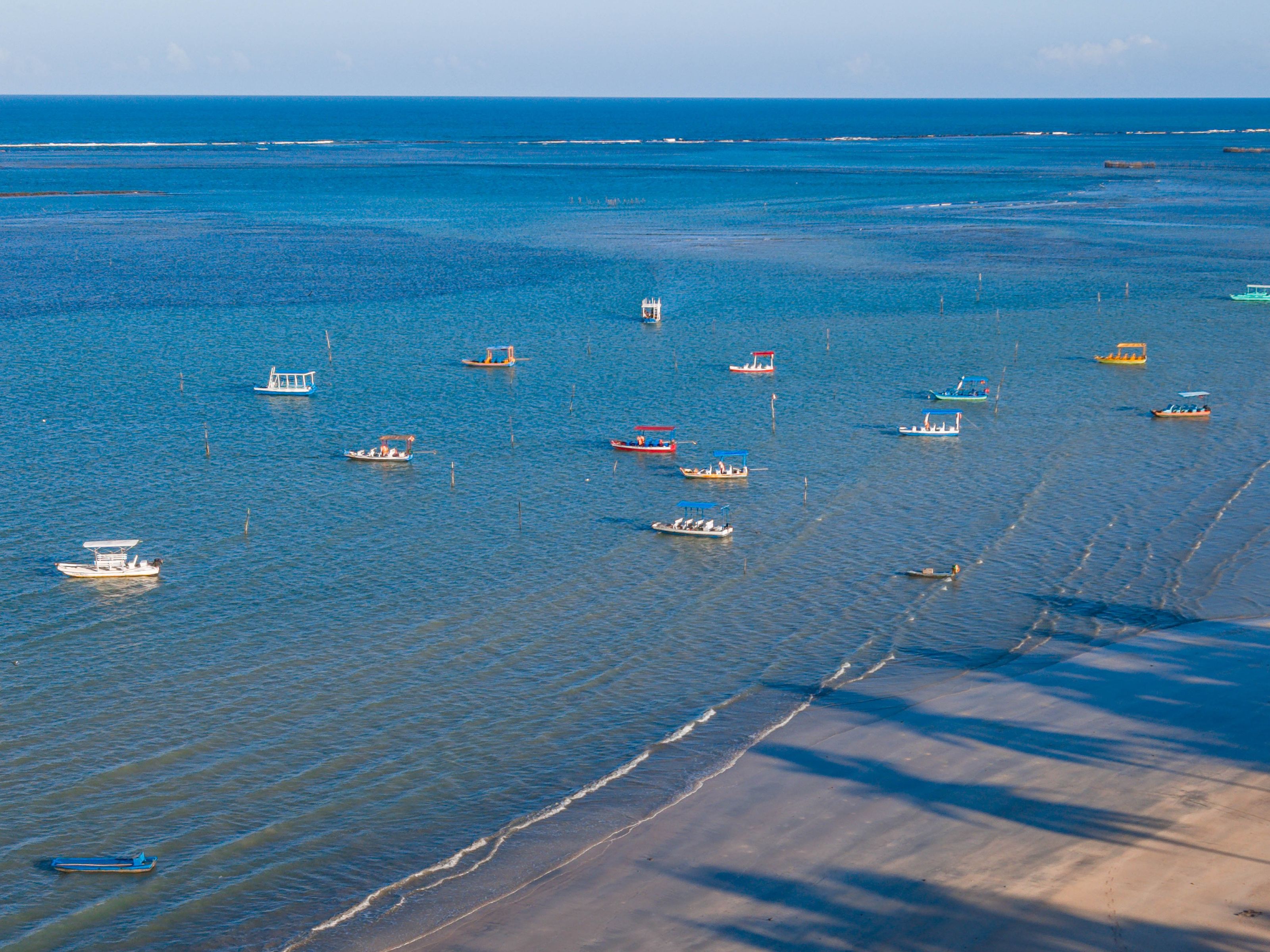 Una zona costera con barcos en aguas tranquilas, una playa arenosa y un cielo despejado.