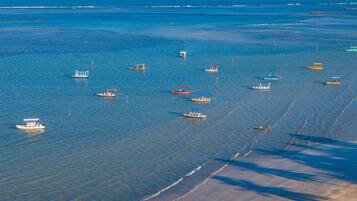 Una zona costera con barcos en aguas tranquilas, una playa arenosa y un cielo despejado.