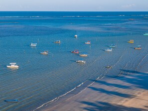 A coastal area with boats on calm waters, a sandy beach, and a clear sky.