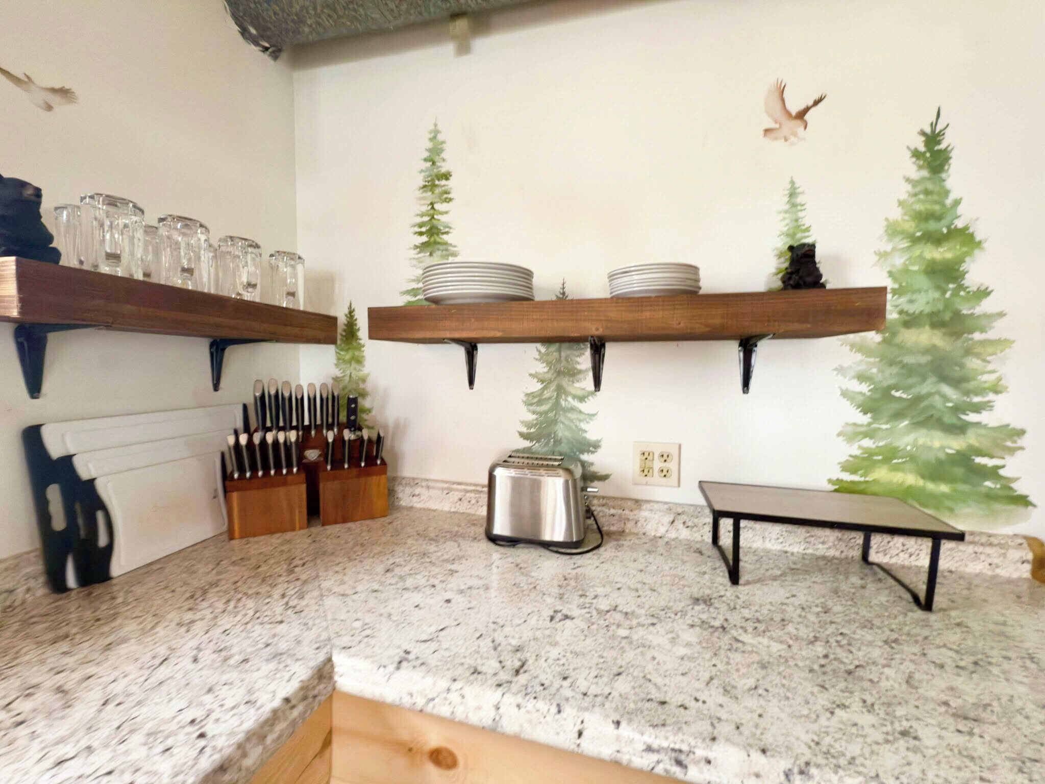 A kitchen with granite countertops, wooden shelves, and a toaster.