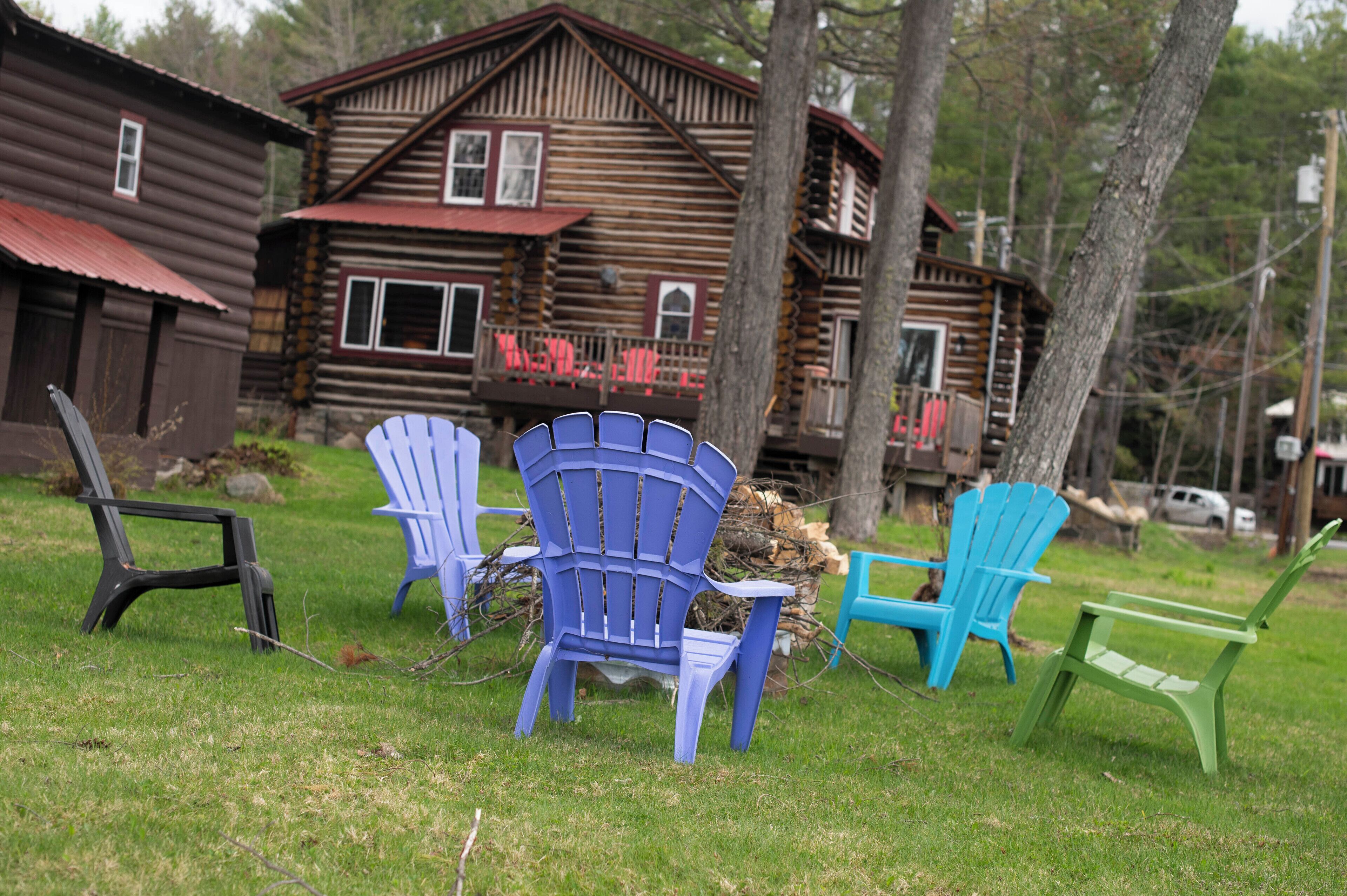 Una cabana de fusta amb un porxo i diverses cadires Adirondack de diferents colors.