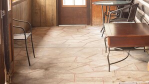 Un intérieur rustique avec des murs en bois, un sol en pierre, une table en bois et des chaises en métal, ainsi qu’une tête de cerf accrochée au mur.