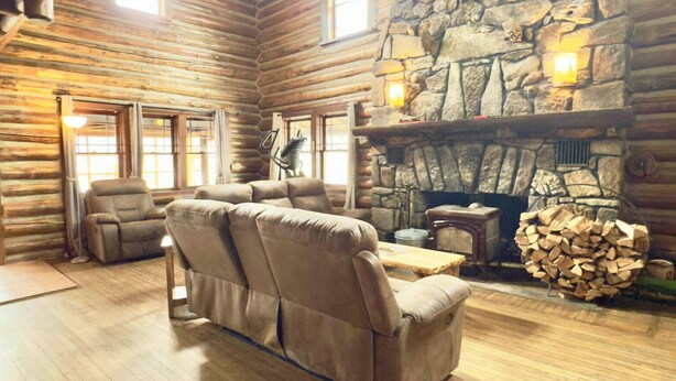 L’intérieur d’une cabane en rondins, avec une cheminée en pierre, des poutres en bois au plafond et un grand canapé en cuir.