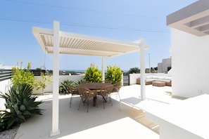 A rooftop patio with a round table and chairs, surrounded by potted plants and a white pergola. - Urb Aloe, 3 bedroom townhouse (Nerja)
