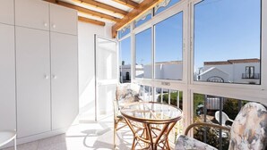 A balcony with a glass table and wicker chairs, white cabinets, and a view of neighboring buildings.