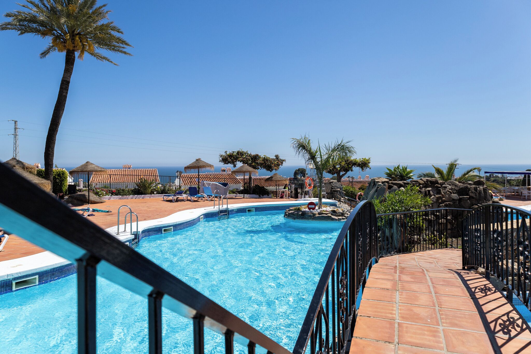 Une piscine entourée d’une terrasse carrelée, de chaises longues, de palmiers et offrant une vue sur la mer.