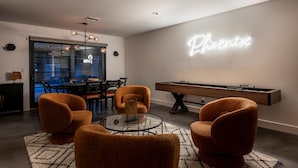 A modern living room with a pool table, orange armchairs, a glass coffee table, and a neon sign on the wall. - Modern Desert Oasis - Shuffleboard, Hiking, Pool & Putting green! (Phoenix)
