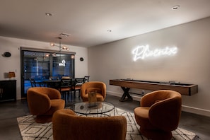 Un soggiorno moderno con tavolo da biliardo, poltrone arancioni, tavolino in vetro e insegna luminosa al neon sulla parete.