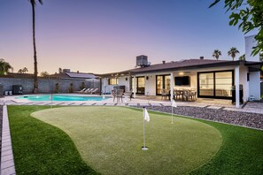 A modern house with a swimming pool, patio furniture, and a well-maintained lawn.