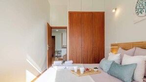 Una cama bien hecha con almohadas y una bandeja con alimentos para el desayuno, un armario de madera y vistas hacia un comedor.