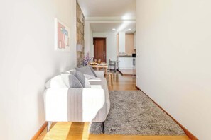 A modern living room with a white sofa, a dining table with chairs, and a kitchen in the background. - Bright & Airy Flat w/ Balcony by HostWise (Porto)