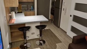 A compact kitchen with wooden cabinets, a granite countertop, two black bar stools, and a built-in oven.