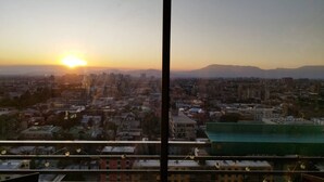 A cityscape at sunset with buildings and mountains in the distance.