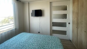 A bedroom with a bed, a TV mounted on the wall, a sliding door, and a window with curtains.