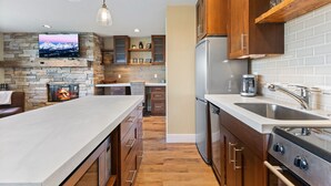 A modern kitchen with a stone fireplace, wooden cabinets, stainless steel appliances, and a large island.