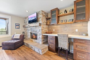 Una sala de estar acogedora con una chimenea de piedra, un sofá cómodo, una zona de comedor con armarios de madera y un televisor sobre la chimenea.