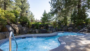 A hot tub surrounded by rocks and trees, with a tiled edge and a metal ladder.