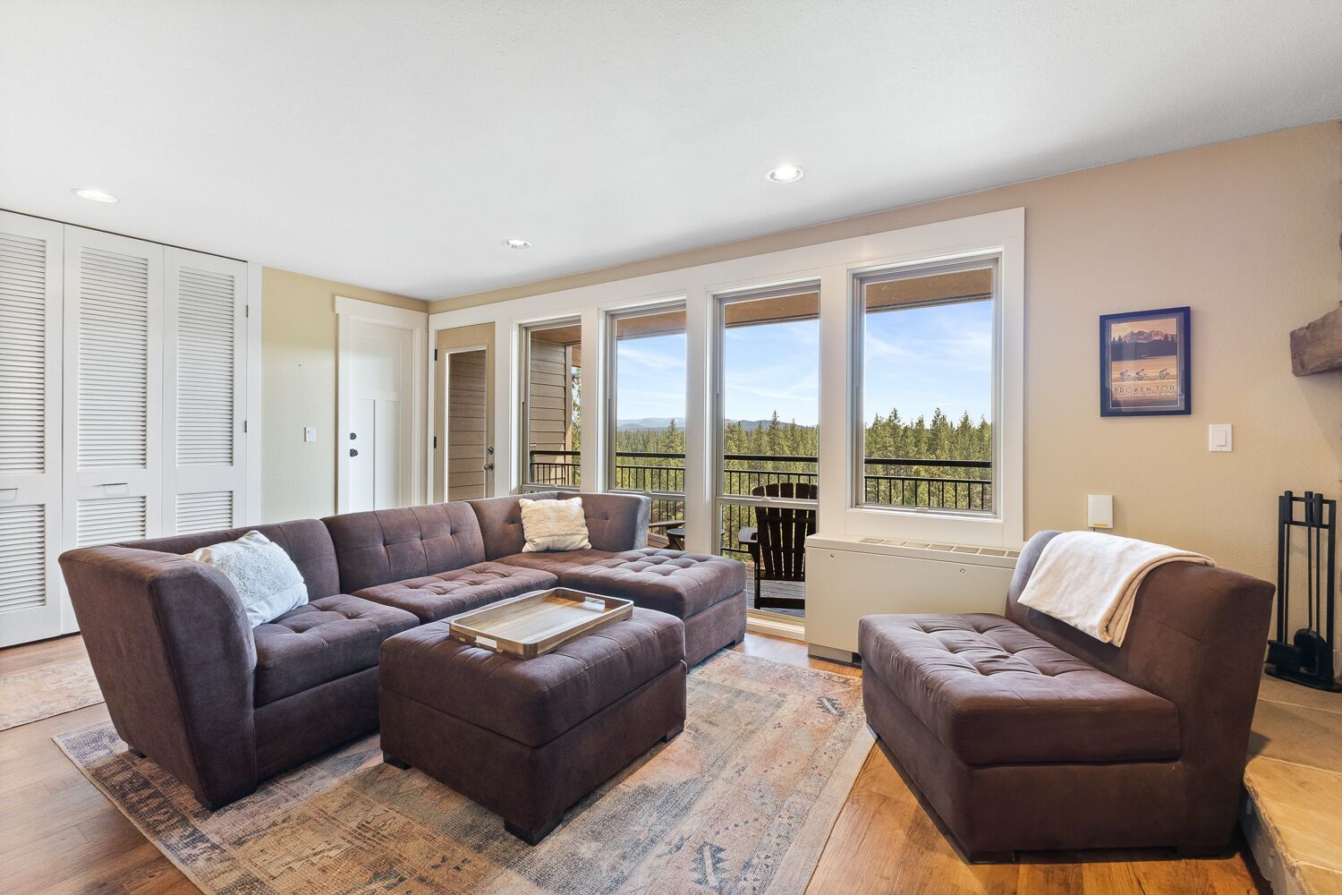 A spacious living room with a sectional sofa, ottoman, and a view of a balcony with a railing.