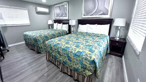 Ein Hotelzimmer mit zwei Betten, jeweils mit einem gemusterten Überwurf, einem Kopfteil, Nachttischen mit Lampen und Bildern an den Wänden.