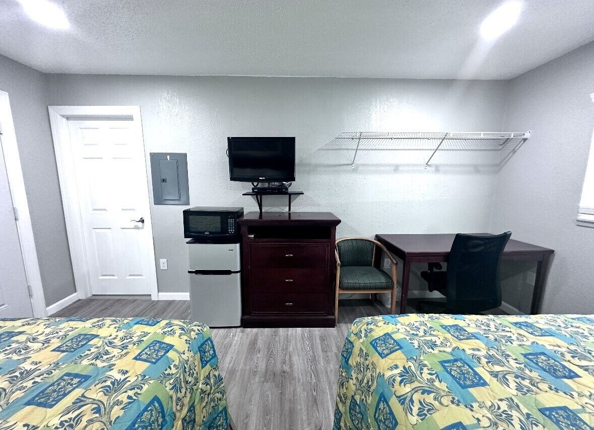 Habitación de hotel con dos camas, un escritorio, televisor, refrigerador y microondas.