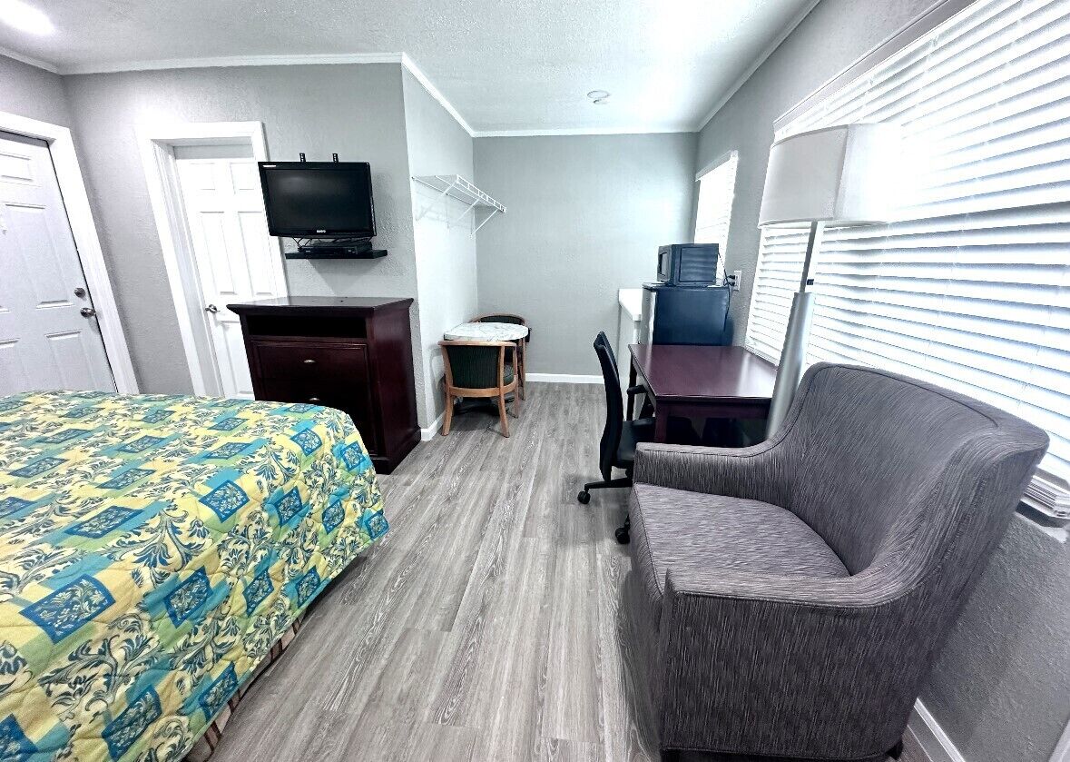 A hotel room with a bed, a desk, a chair, a television, and a window with blinds.