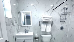 Ein Badezimmer mit Marmorwand, Toilette, Waschbecken und Duschbereich.