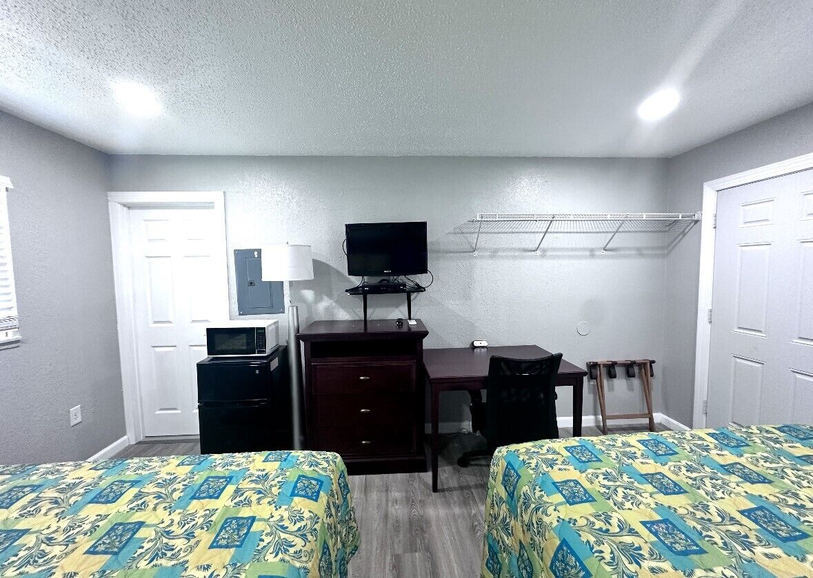 A small, clean room with two beds, a desk, a chair, a TV, and a clothes drying rack.