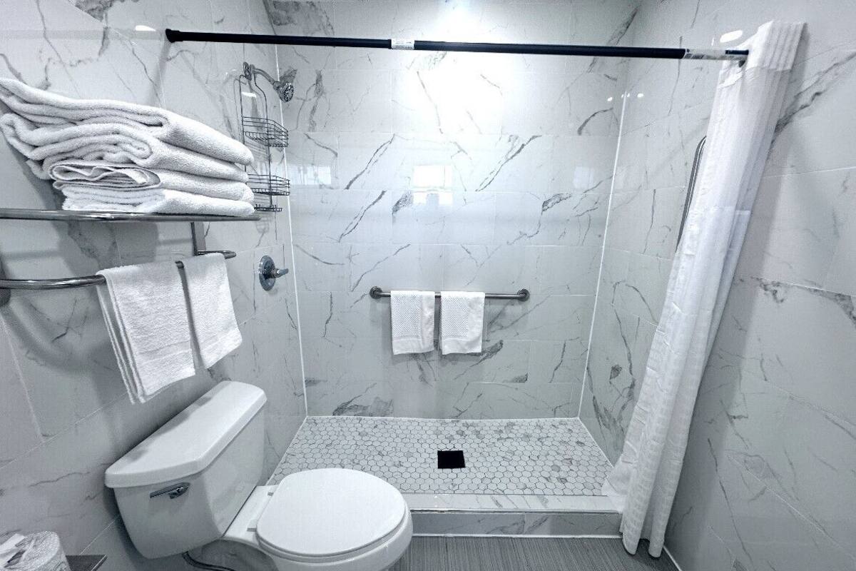 A modern bathroom with a glass-enclosed shower, marble walls, and a toilet.