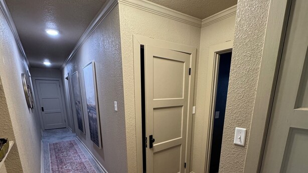 A hallway with wooden flooring, beige walls, and a ceiling light fixture.