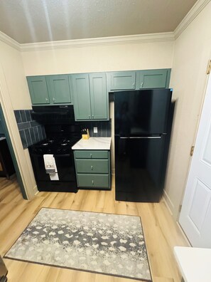 A compact kitchen with teal cabinets, a black refrigerator, and a patterned rug. - Charming 3-bedroom house w/WiFi, close to Highland Industrial Park- East Camden (East Camden)