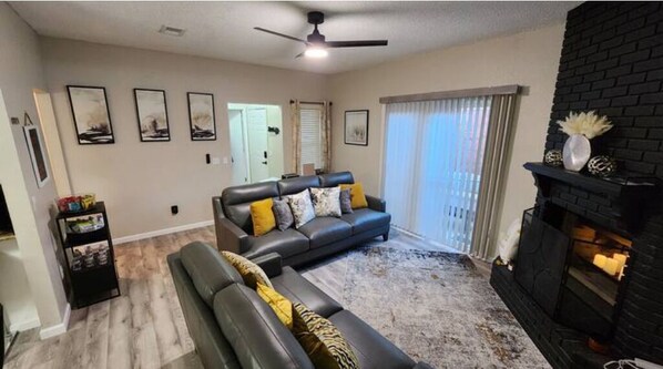 A living room with a sofa, a fireplace, and a ceiling fan. - Cozy in Sooner Land (Norman)