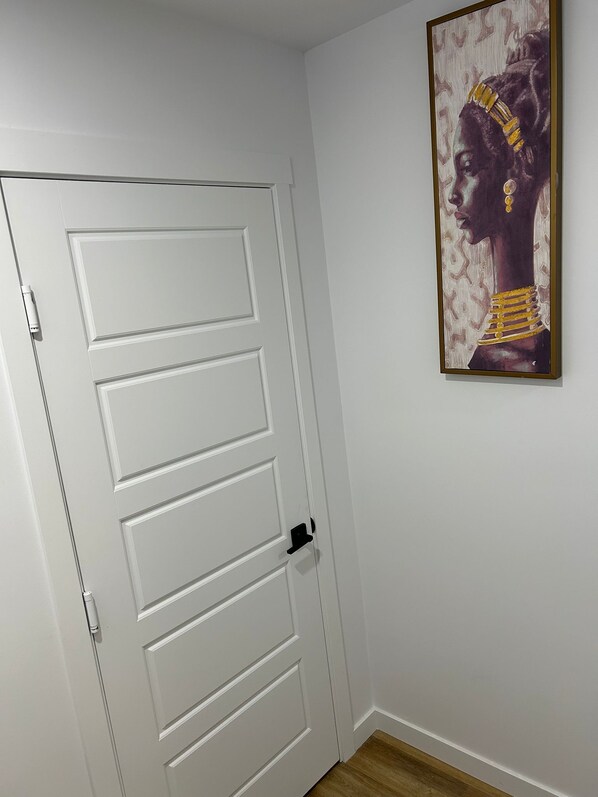 A white door with a modern handle, a framed artwork on the wall, and a wooden floor.