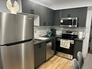 A modern kitchen with stainless steel appliances, a marble backsplash, and a wooden floor.