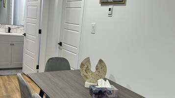Un coin repas comprenant une table en bois, des chaises à revêtement gris, un élément décoratif mural et un tableau.