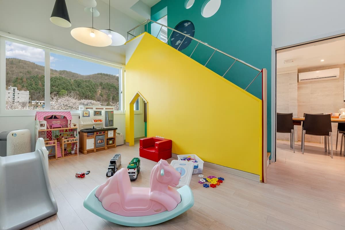 Un cuarto de juegos infantil luminoso y moderno con un gran ventanal, una cocina de juguete y un tobogán.
