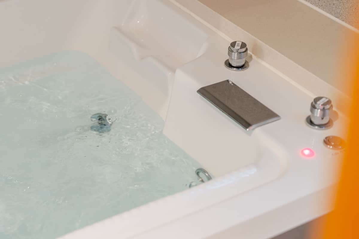 Una bañera con sistema de hidromasaje, un mando de control y un indicador luminoso rojo.