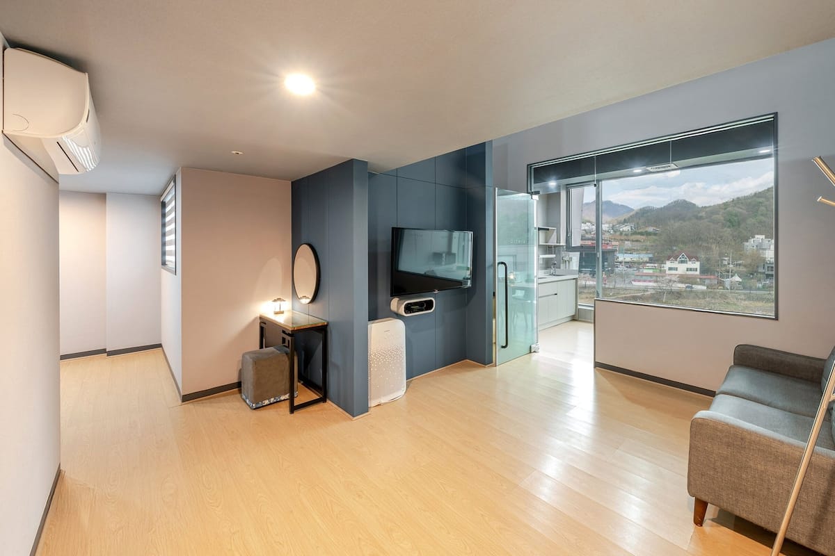 Una sala de estar moderna con un ventanal grande, un televisor de pantalla plana, un sofá y una kitchenette pequeña.