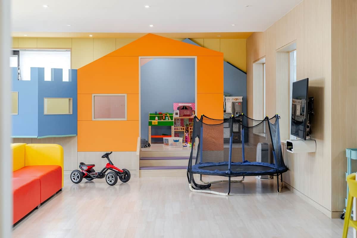 Una sala de juegos muy colorida con un trampolín, una triciclo rojo y un sofá rojo.